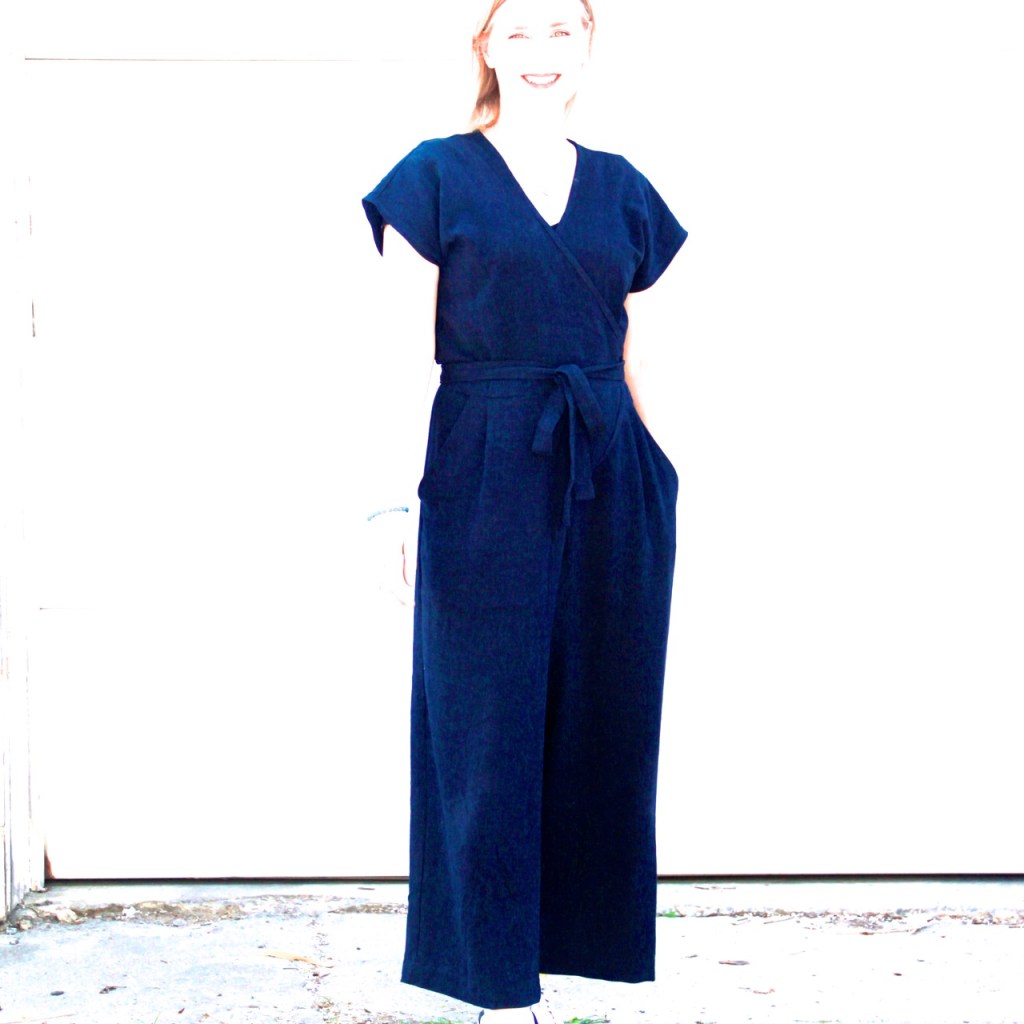 Lori stands smiling wearing a navy blue jumpsuit that wraps at the front and has a tie belt. The photo is completely over-exposed so you can barely see Lori but the blue jumpsuit is clearly visible.